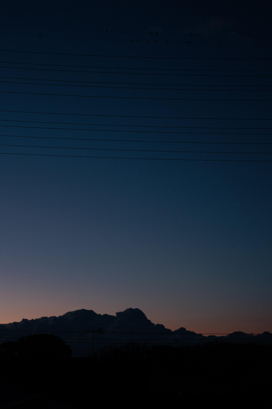 Silhouetted clouds against a darkening sky, with power lines and birds perched above.