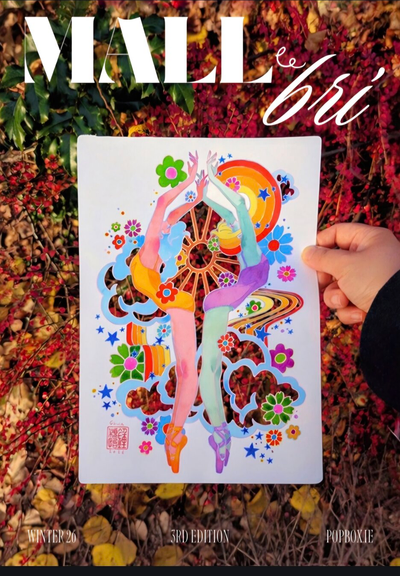 Photograph of the 3rd issue covee of Mall le Brí magazine. It's colorful, abstract pop-art drawing held by a hand against a background of autumn leaves and red bushes. The drawing features two dancing, abstract dancers in pastel colours, intertwined with vibrant flowers, stars, and a sun-like circle.