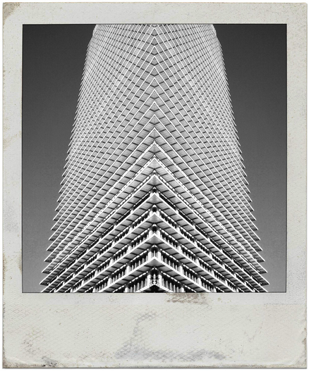 A black and white photo showing a low angle view of a 1960s era high rise building, full of sharp angles.