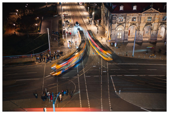 Blick von oben auf eine Kreuzung. Drei Straßenbahnen fahren durch das Bild und sind durch ihre Bewegung unscharf.