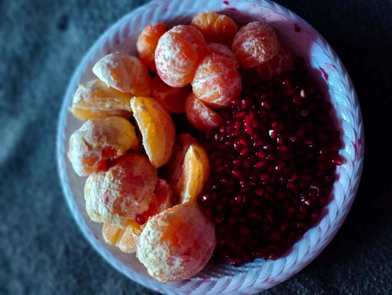 A bowl of fruit, composed of peeled mandarin oranges and pomegranate seeds, arranged on a textured white plate.