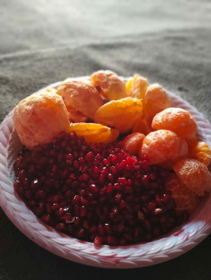 Close-up of a white plate with a carved rim, containing peeled orange mandarin segments and a mound of bright red pomegranate seeds.