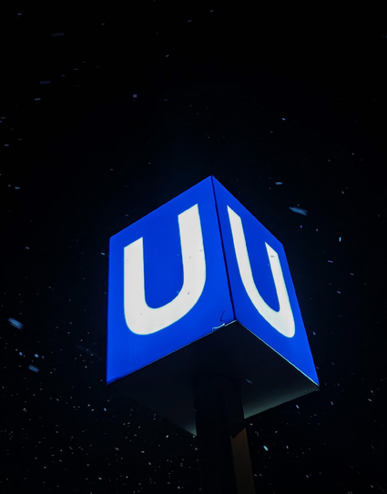 A photo of a blue illuminated subway sign with white “U”, in the dark with a light snow fall.