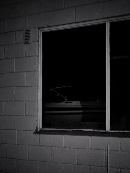 A boat inside a warehouse, only  visible through the window, because of a streetlight nearby. The picture is b&w