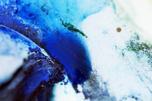 Nahaufnahme von blauen Farbresten in einer Palette. Die angetrocknete Farbe wechselt von sattem Dunkelblau links in einem Farbverlauf zu weißblau rechts. Der Fokus liegt auf einer Kante des Farbtöpfches, das Bild ist abstrakt.

Close-up of blue paint residue in a palette. The dried paint changes from a rich dark blue on the left to a white-blue on the right. The focus is on one edge of the paint pot; the image is abstract.