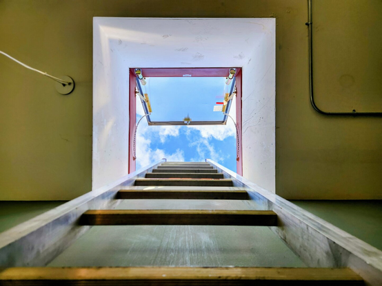 a shot from below of a ladder leading up to an open roof hatch