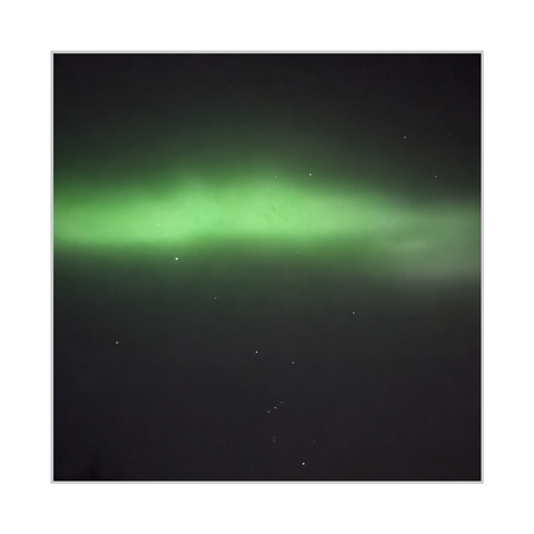 Square color photograph. A dark night sky fills the frame, with a broad, soft band of green aurora stretching horizontally across the middle and fading into darker tones above and below. Scattered stars are visible throughout. Near the lower edge, the Orion constellation appears as a compact group of brighter points, including the three aligned belt stars and a small vertical cluster below them.