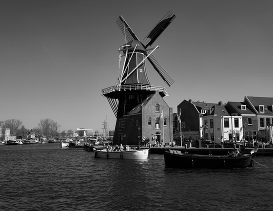 view of a large canal and a large windmill on its banks. Boats and occupants are in the foreground and background