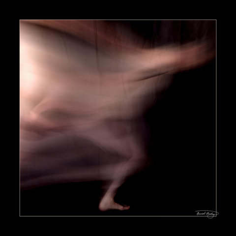 Square image with black frame and black background showing a naked person running from left to right. The person is greatly blurred due to a long exposure time. Only one foot is in focus.