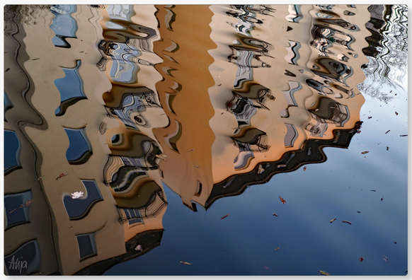 Reflexion von einem Haus mit apricotfarbenem Anstrich und vielen Fenstern und Balkonen in einem Kanal mit bläulich wirkendem Wasser, alles scheint in Bewegung, fließende Linien zaubern schöne Effekte.

Reflection of a house painted apricot with many windows and balconies in a canal with bluish water; everything seems to be in motion, flowing lines conjure up beautiful effects.