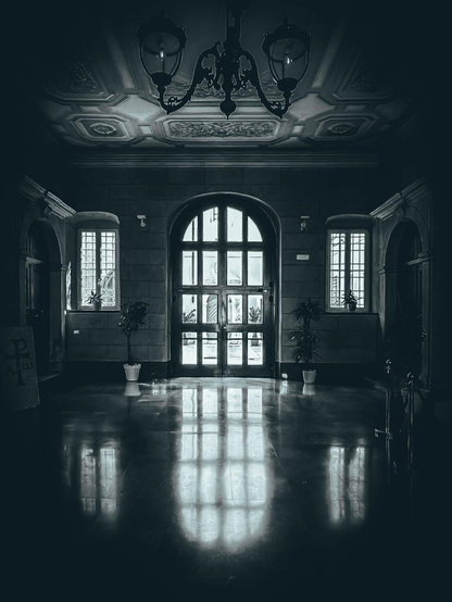 Eine Eingangshalle mit einer großen gewölbten Tür am Ende. Der Raum verfügt über eine dekorative Decke, Kronleuchter und Topfpflanzen. Reflexionen sind auf dem polierten Boden sichtbar

An entrance hall with a large arched doorway at the end. The space features a decorative ceiling, chandeliers, and potted plants. Reflections are visible on the polished floor.