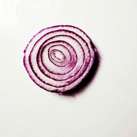 A high contrast color photo of an almost circular slice of a red onion where you can see the pattern and texture in close-up.
