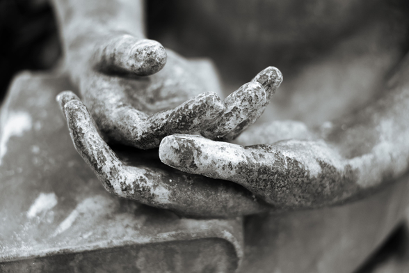 Schwarzweiße Nahaufnahme von Händen einer Grabfigur. Die übereinanderliegenden Hände liegen auf einem Buch. Eine (grüngraue) Patina aus Flechten hat die Figur besiedelt.

Black-and-white close-up of the hands of a grave figure. The hands are placed one on top of the other on a book. A (green-grey) patina of lichen has colonised the figure.