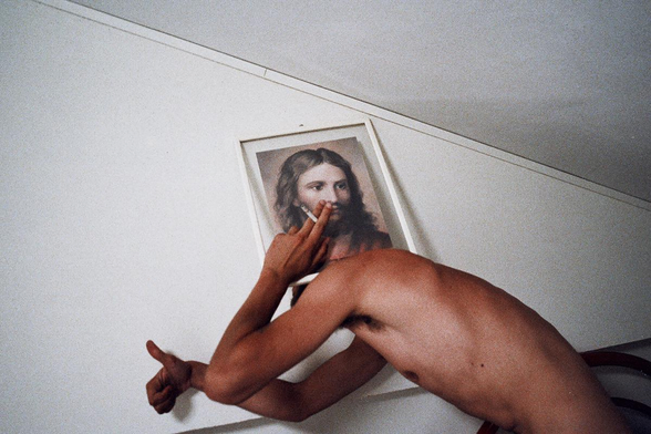 la photographie du christ sur un torse nu d’homme portant une cigarette à Sa bouche et faisant signe de l’autre main que tout va bien