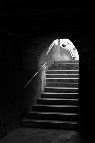 Steps rise out of the dark; a little bridge framed under an arch.