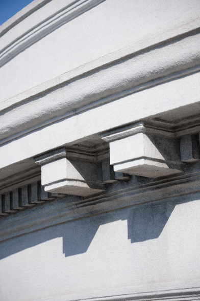 Close-up of architectural details featuring shadowed angular protrusions and textured surfaces on a grey stone facade against a blue sky.