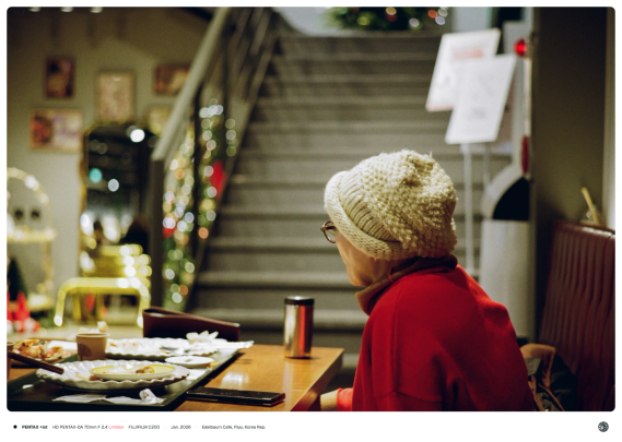 붉은 옷을 입은 노인이 카페 테이블에서 일행을 기다리고 있는 모습.