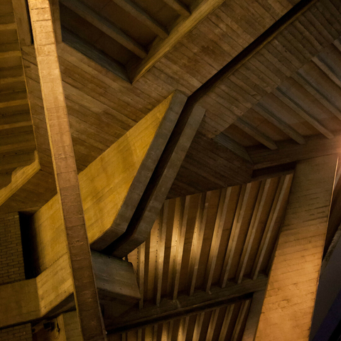 Photo looking up at many and varied angular concrete ribs and brackets under an elevated brutalist building, all coloured by amber light.