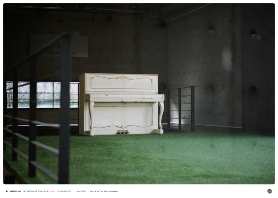 바닥이 초록색인 빈 사무실 한 가운데에 흰색 피아노만 덩그러니 있는 모습.