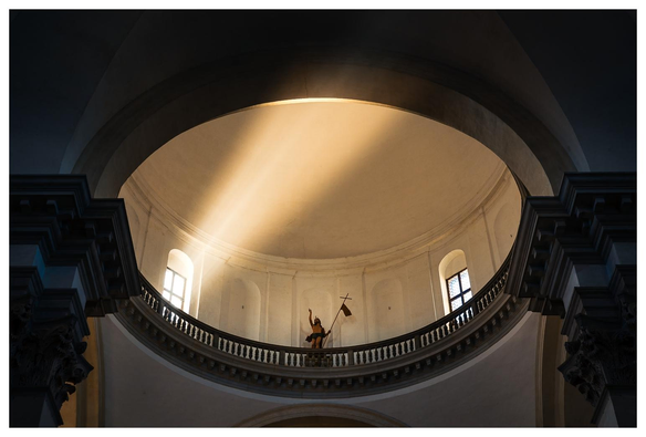 Blick in die Kuppel einer Kirche. Durch ein Fenster fällt Licht und streut in der weihrauchigen Luft.