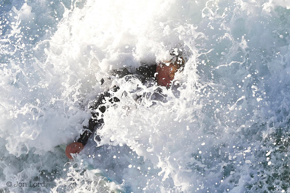 This is a colour water sports photo in landscape format of a surfer overwhelmed by the surf of a breaking Pacific wave. Hermosa Beach, California (2016).

In the centre of the image is a faint and close-up view of a male surfer who is covered in the brilliant white, foaming surf of a large breaking wave. The surf covers the entire frame with only the outline of our surfer in the centre. The intrepid surfer is viewed in profile, and is placed, for a moment, diagonally across the photo, head towards the upper right corner and right hand towards the lower left. Thats about all thats visible - well he has blond or ginger hair, eyes clamped shut, is wearing a black wetsuit and possesses a right arm and hand - thats it, thats all thats visible, just surf - lots of surf.

Oh, in case you wondered, he survived: thought nothing of it, swam back with his board to meet the next wave.