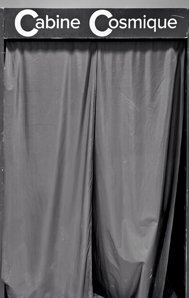 A photo of some sort of booth with a sign reading "Cabine Cosmique" above closed curtains that cover the entrance.
