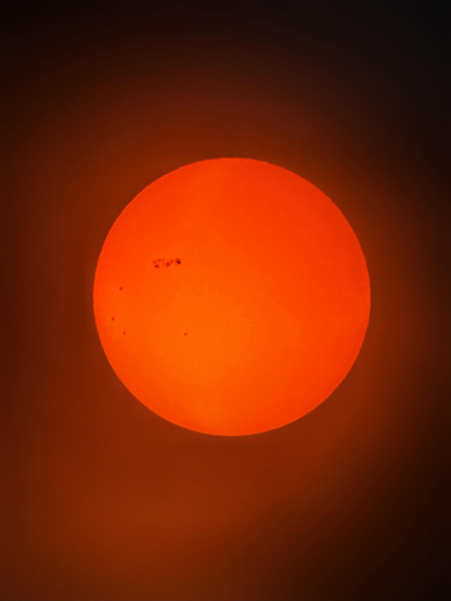 Photo of the sun taken a few days earlier with the same equipment. In this photo the sun has a more reddish hue. The sunspots are on its northwestern quadrant and appear less prominent.