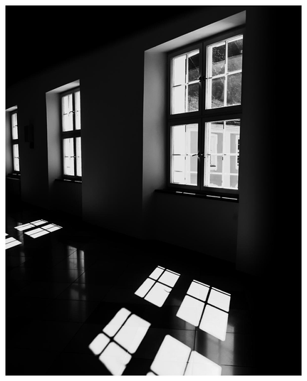 Unterbelichtetes Foto von Fenstern durch die gleißend helles Licht fällt. Die Sprossen bzw. Fensterfelder werden scharf als Licht und Schatten auf den Boden projiziert.