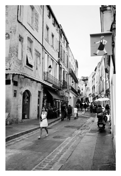 a young woman dressed in white walking down the street next to a shop sign featuring a stylized baker having nearly the exact same posture