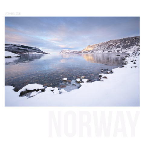Snowy shoreline along the fjord with pink and orange clouds catching the light above.