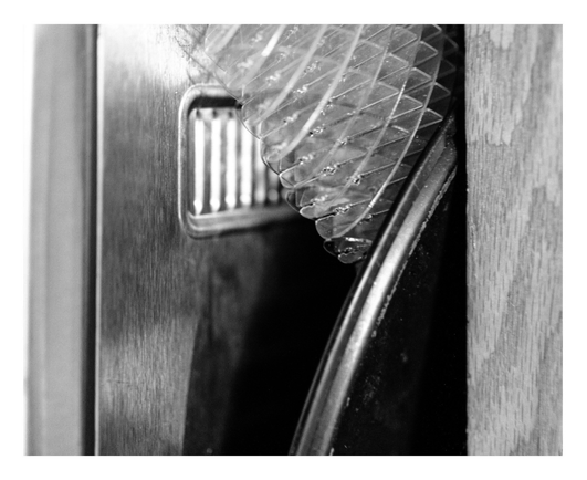 Black-and-white close-up of a plastic hose wedged between metal and wood surfaces.