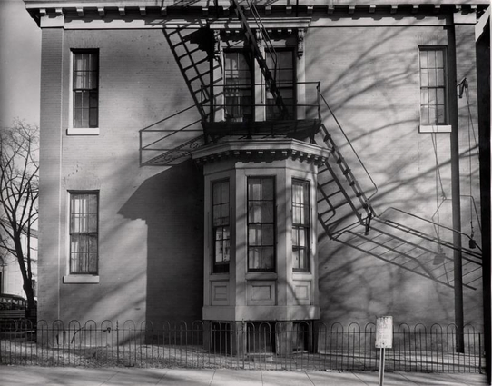 des ombres dessinent vaguement des ailes de moulin sur la façade d’une maison