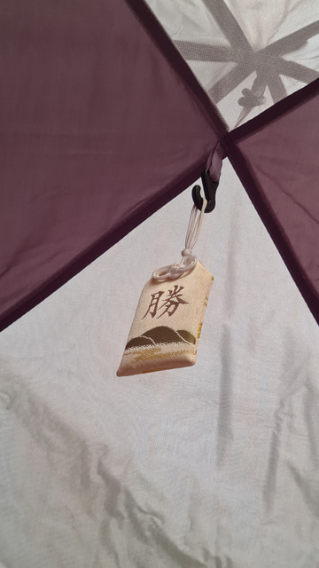 A close up of a tiny Japanese bag of luck. It's hanging from the hook at the center of a tent.
