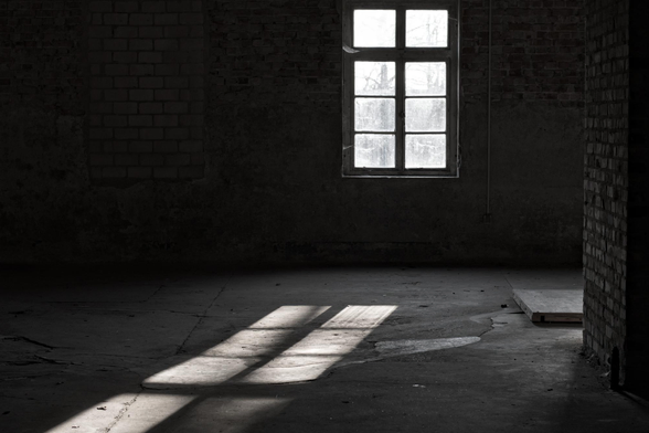Fenster mit Lichtstrahlen, die auf einen leeren, dunklen Raum mit Betonboden und Backsteinwänden fallen