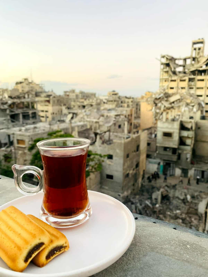 A glass of tea and two cookies on a white plate are set against a backdrop of a war-torn city.