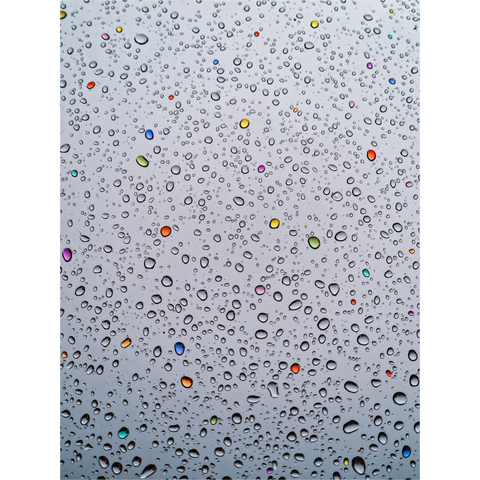 A photo of a grey window pane covered in water droplets of varying sizes and shapes. The light reflects off the curved surfaces of the droplets, creating bright highlights along their edges. Interspersed among the clear water droplets are a few that are coloured in red, orange, yellow, green, blue and purple.