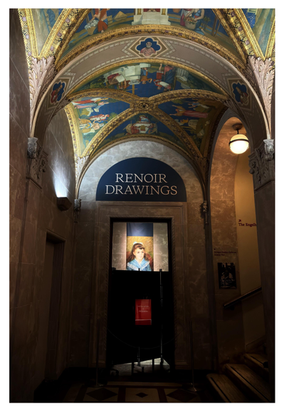A hallway inside the Morgan Library and Museum in New York. Marble walls rise up to a groin-vaulted ceiling with elaborate ornamentation and Renaissance-themed imagery. An overhead lamp illuminates a stairway leading off to the right. In the middle of the photo is a doorway under a lunette with large text that reads “RENOIR DRAWINGS.” Through the doorway we can see a banner with an artwork reproduction hanging on a far wall: Pierre-Auguste Renoir’s “Portrait of a Girl (Elisabeth Maître),” featuring a brown-haired girl in a blue dress. The lower part of the banner is blocked from view by dark folding screens and a small red sign that says “INSTALLATION IN PROGRESS.” A rope barrier between two stanchions further discourages entry.