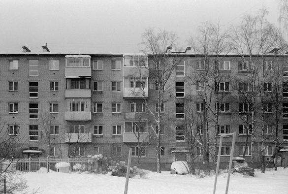 The black-and—white photo shows a Soviet five-story building ("Khrushchev"), and in front of it is a snow-covered courtyard.