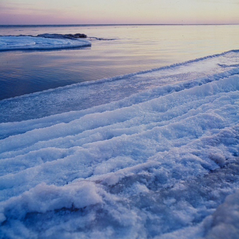 The Baltic Sea in winter, at dusk. In the foreground, piles of frozen snow and ice; in the distance, the blurred sea.