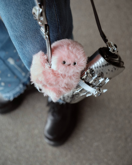 A  robot with wide eyes and soft pink fur, which clutches onto stylish handbags and shyly glances around.