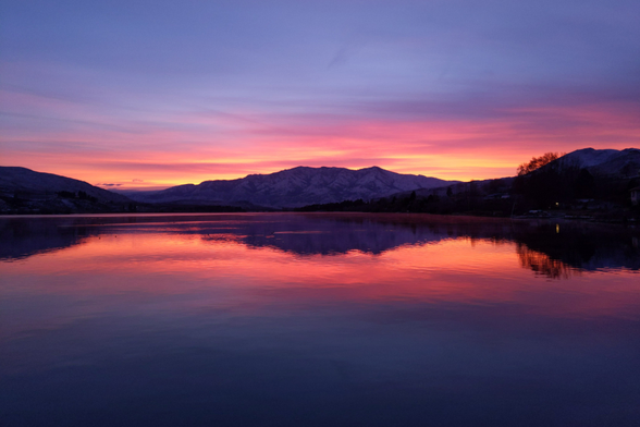 The sky after sunset, or civil twilight, very red, reflecting off the calm water where there are some duck like birds. There is snow on the mountain