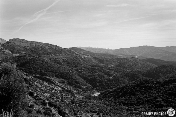 A black and white panoramic view of rolling hills and mountains, showcasing lush vegetation and varying terrain under a clear sky, capturing the serene beauty of a natural landscape.