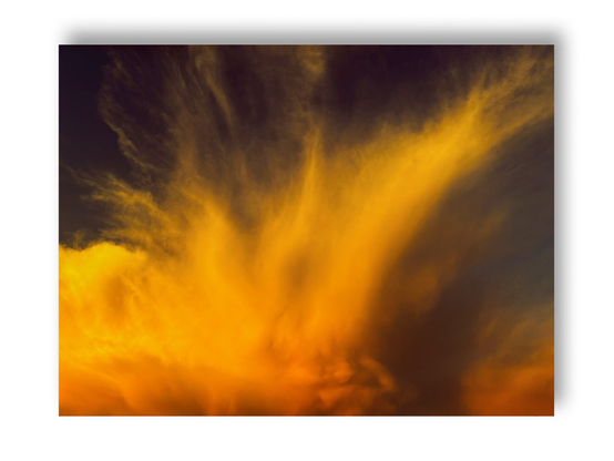 A color photo of dramatic clouds lit by the setting sun. Framed in white.
