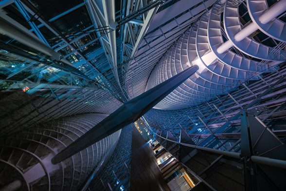 Reflection shot with titled angle inside Tokyo International Forum at night. The reflected architectural elements evocate a science fiction spaceship making its way through futuristic towers. The gigantic modern architecture and blueish and purple lights in the shadow of the night add to the cyberpunk atmosphere.
