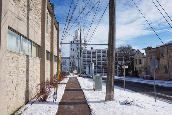 Standing on a sidewalk next to a large courthouse a tall processing plant (Quaker Oats) can be seen in the distance. Snow can be seen on the ground and a road with other buildings is on the right on this sunny day.