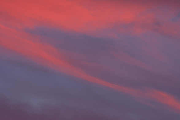 Distant cirrus clouds capture the setting sun's orange-pink light and make an abstract pattern of reds, middle blues, and dark blue-gray. 