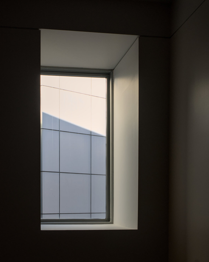 The view through the window is only of a white tiled wall, partly in sun and partly in shade