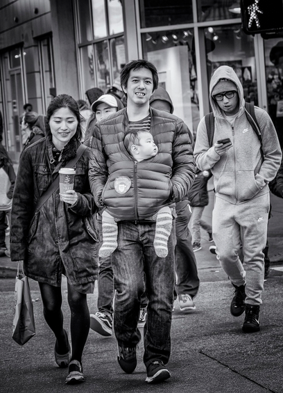 Couple walks across the street in the North Beach neighborhood of San Francisco. The man has a baby in a holder against his chest.