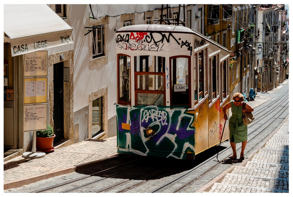 Eine unbeugsame ältere Dame latscht neben einer kleinen Standseilbahn eine recht steiel Straße hinauf.