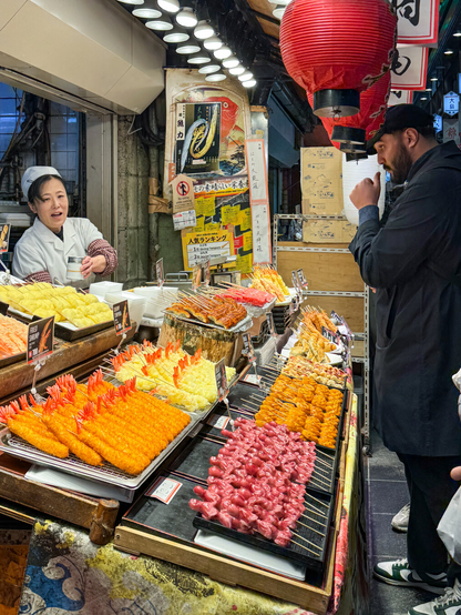View of a public market vendor booth showing numerous fried meats-on-a-stick items.